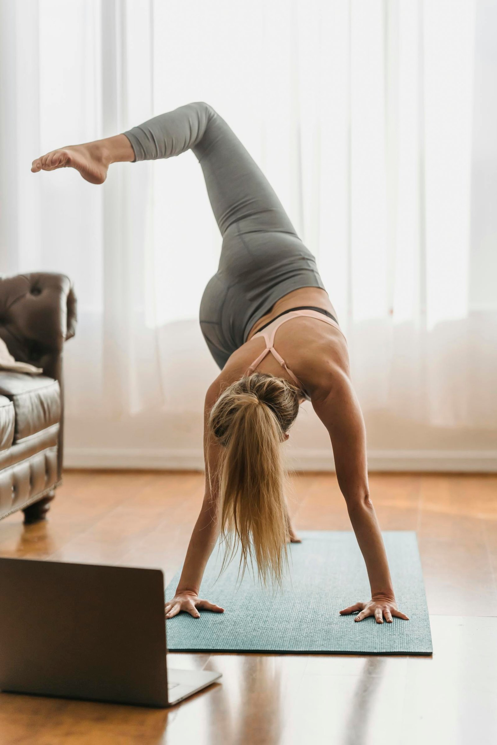 Full body of faceless barefoot female in sportswear performing eka pada svanasana posture on mat near laptop during online yoga training